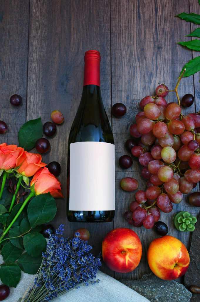 A vibrant display of wine, fresh grapes, peaches, and roses on a wooden surface.